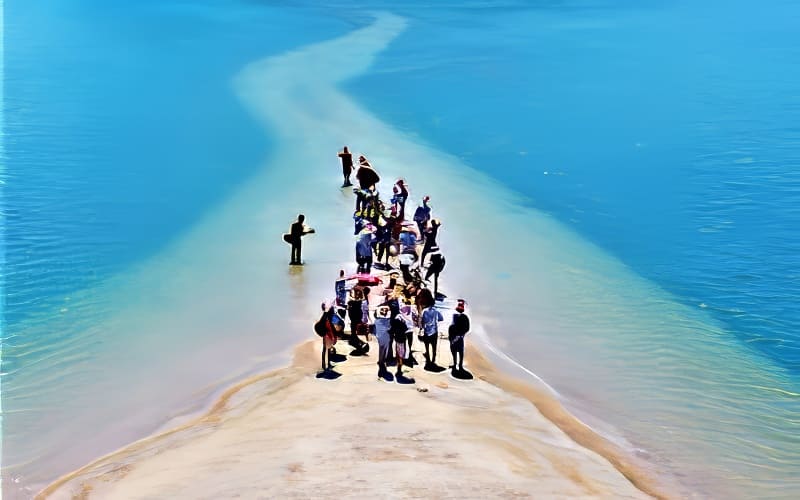 Kỳ thú những cung đường bộ xuyên biển Một nhóm người tụ tập trên một dải cát hẹp bao quanh bởi làn nước xanh thẳm dưới bầu trời trong xanh. Khung cảnh vui tươi này truyền tải cảm giác phiêu lưu và khám phá.