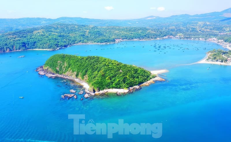 Kỳ thú những cung đường bộ xuyên biển - Ảnh 11. Ảnh chụp từ trên cao cho thấy một hòn đảo xanh tươi tốt được bao quanh bởi làn nước trong xanh, với những ngọn đồi xa xa và những chiếc thuyền rải rác ở phía sau.