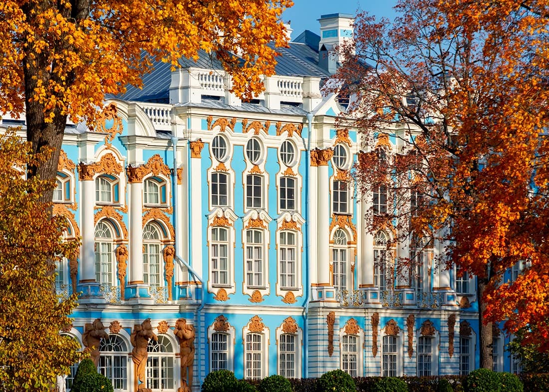 Mặt tiền cung điện trang trí công phu với tông màu xanh lam và trắng điểm xuyết vàng, được bao quanh bởi những tán cây mùa thu rực rỡ sắc cam, toát lên vẻ thanh lịch và quyến rũ dưới ánh mặt trời.